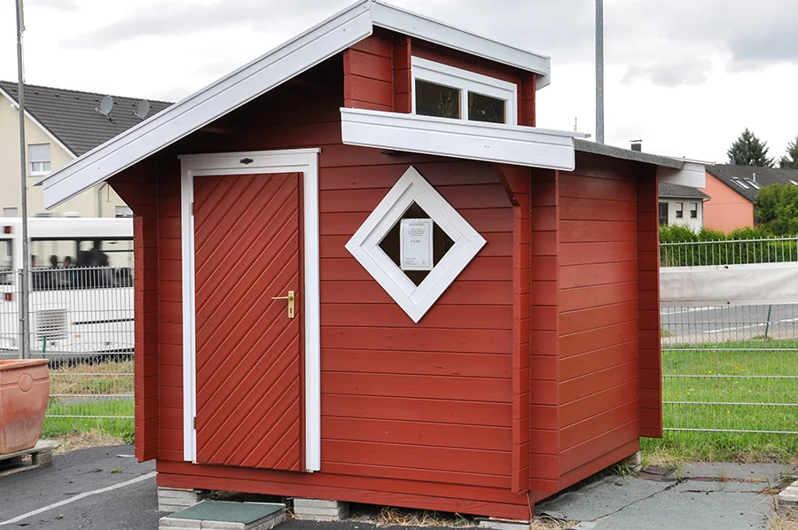 rot lackiertes Holz Gartenhaus mit Stufendach. Fensterrahmen und Dachelemente weiß lackiert.