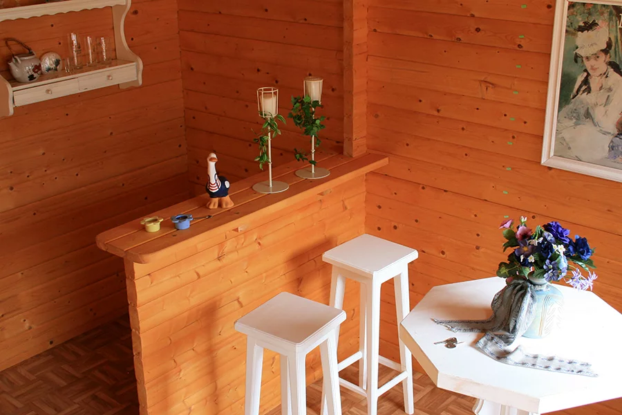 Innensicht Gartenhaus. Holztresen mit zwei weiß lackierten Barstühlen. Davor: Weißer, achtkantiger Tisch