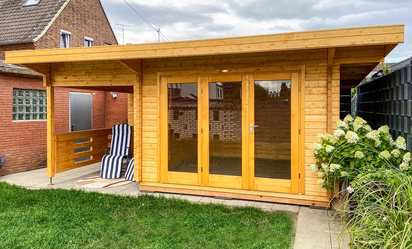 Holz Gartenhaus mit dreigliedrig verglaster Tür und verlängertem Pultdach. Unterstand mit zwei Liegestühlen auf der Seite